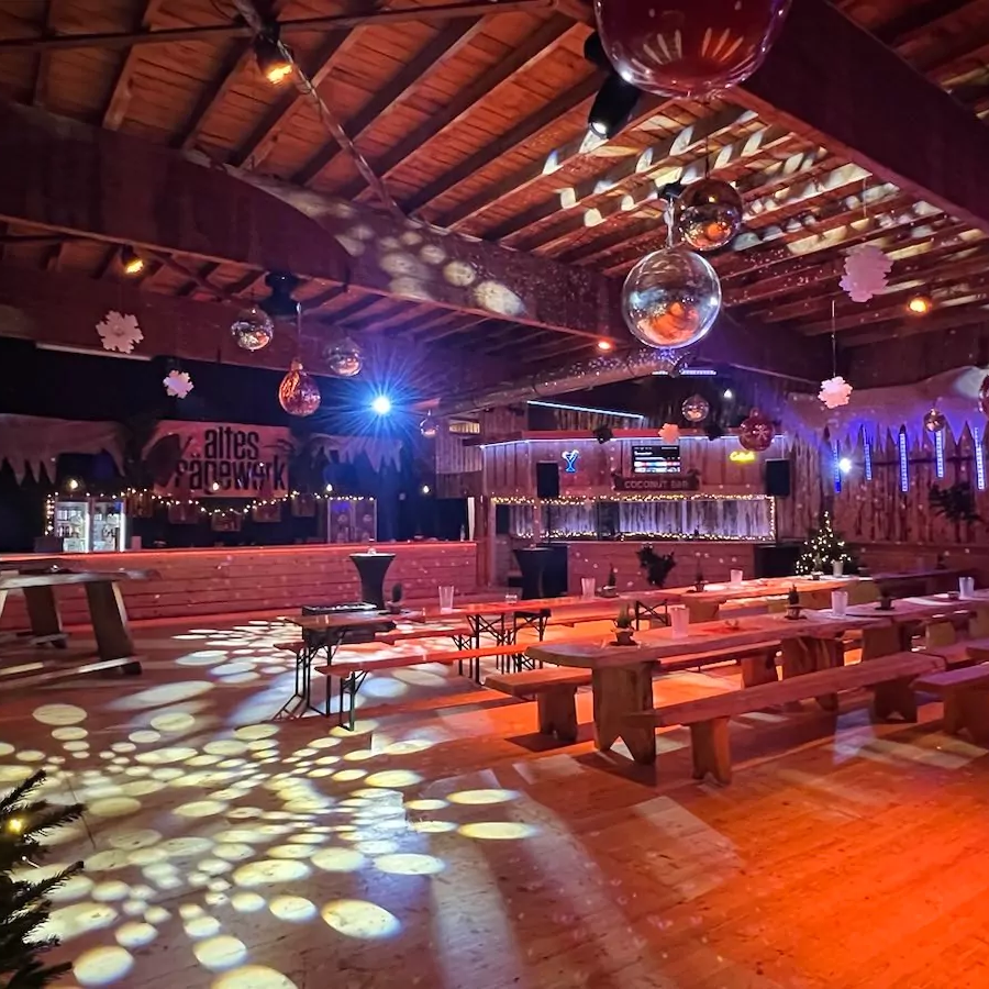 Location Ein festlich dekorierter Veranstaltungsraum mit Holzdecke und bunten Lichtern.