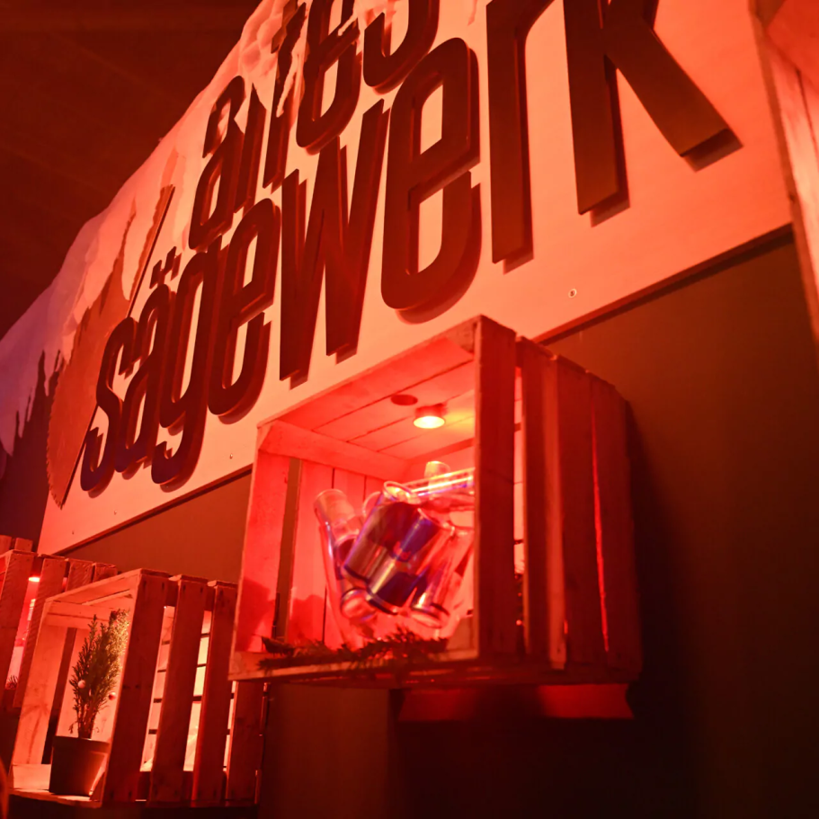 Kontakt Rote Beleuchtung und Holzkisten vor einer Wand mit der Aufschrift "Sägewerk".