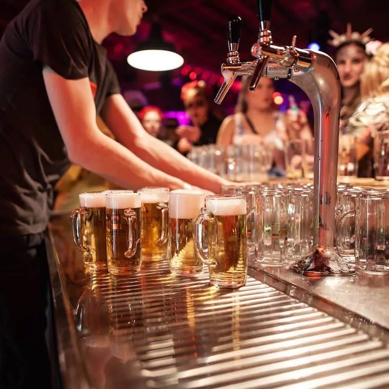 Altes Sägewerk Eine Bar mit mehreren vollen Biergläsern und einem bietenden Barkeeper.