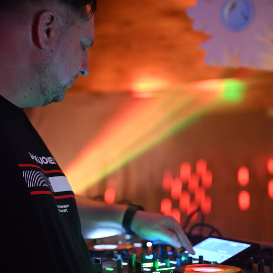 DJ Thomas Ein DJ steuert ein Mischpult mit bunten Lichtern im Hintergrund.